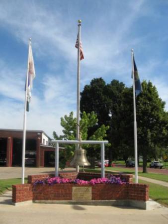 Arkansas City 9/11 Memorial; 3 flag posts, bell, flowers, and plaque